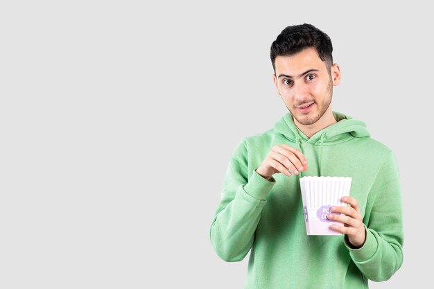Porträt eines jungen Mannes im Sweatshirt, der Popcorn über Weiß isst