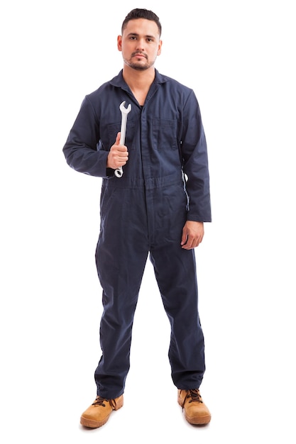 Porträt eines jungen Mechanikers, der Overalls trägt und einen Schraubenschlüssel bei der Arbeit auf weißem Hintergrund hält