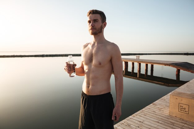 Porträt eines jungen müden Sportlers, der Wasser nach dem Joggen trinkt