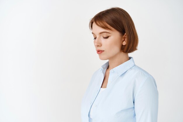 Porträt eines jungen natürlichen Mädchens mit kurzen Haaren, das eine blaue Bluse trägt, die nach unten schaut und seitlich auf weißem Hintergrund für Ihr Logo steht