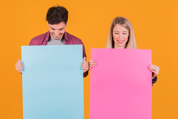 Kostenloses Foto porträt eines jungen paares, das blaues und rosa plakat gegen einen orange hintergrund betrachtet