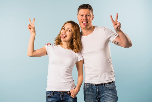 Porträt eines jungen Paares, das heraus ihre Zunge zeigt Friedenszeichen haftet