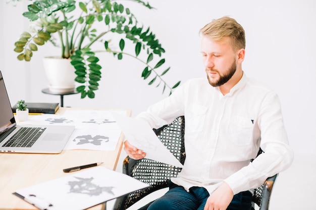 Kostenloses Foto porträt eines jungen psychologen, der rorschach-inkblot-testpapier im büro betrachtet