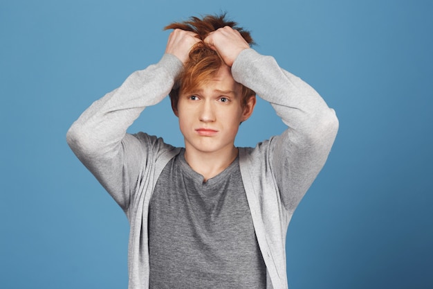 Kostenloses Foto porträt eines jungen rothaarigen studenten in freizeitkleidung, die haare mit den händen hält und nach einem anstrengenden studientag kopfschmerzen hat. kerl fühlt sich schlecht wegen trennung mit freundin.