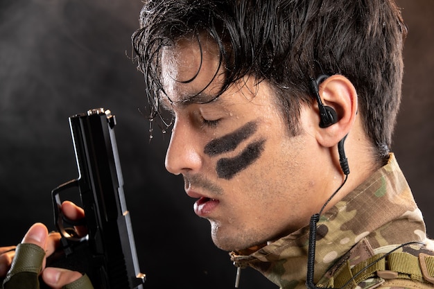 Porträt eines jungen Soldaten in Tarnung, der eine Waffe an der schwarzen Wand hält