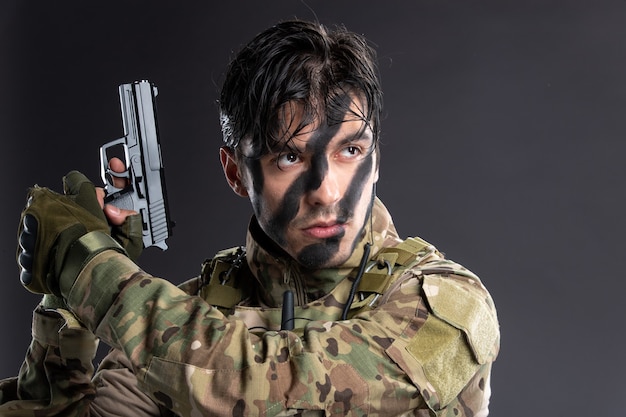 Kostenloses Foto porträt eines jungen soldaten in tarnung, der mit einer waffe auf eine dunkle wand zielt