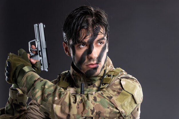 Porträt eines jungen Soldaten in Tarnung, der mit einer Waffe auf eine dunkle Wand zielt