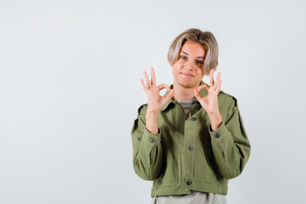 Kostenloses Foto porträt eines jungen teenagers, der ein gutes zeichen in der grünen jacke zeigt und eine fröhliche vorderansicht sieht