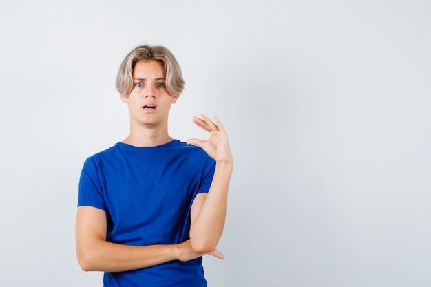 Porträt eines jungen teenagers, der ein kleines schild im blauen t-shirt zeigt und eine schockierte vorderansicht zeigt