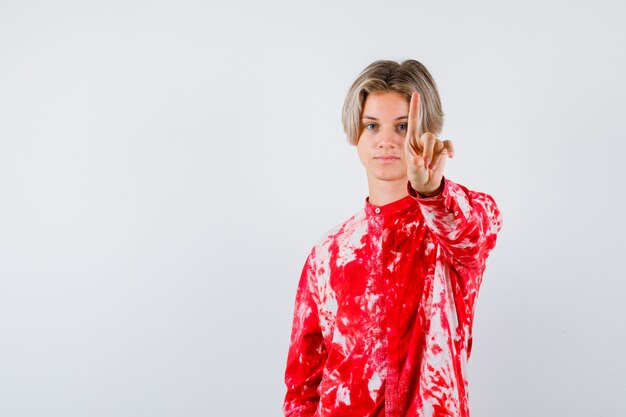 Porträt eines jungen Teenagers, der eine winzige Geste im Hemd hält und eine ernsthafte Vorderansicht sieht