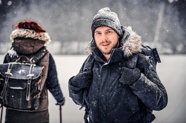 Porträt eines jungen Wanderers mit Rucksack, der mit seiner Freundin durch einen Winterwald geht