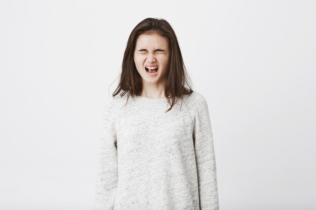 Porträt eines kindischen Teenagers, der im Begriff ist zu weinen, mit geschlossenen Augen steht und laut schreit.