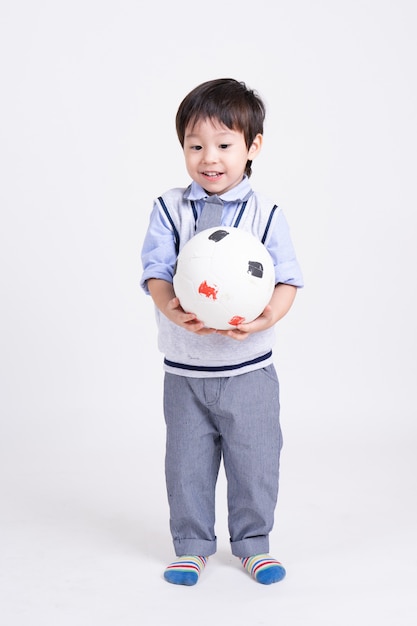 Porträt eines kleinen Jungen, der mit dem Lächeln in der Hand hält Fußball steht