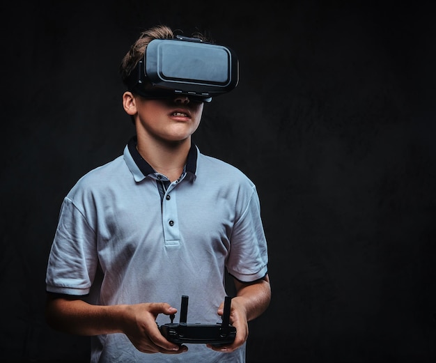 Porträt eines kleinen Jungen in einem weißen T-Shirt mit einer Virtual-Reality-Brille und einer Fernbedienung. Getrennt auf dem dunklen Hintergrund.