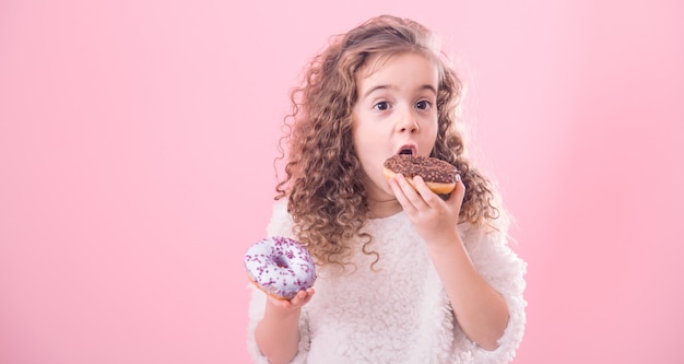 Porträt eines kleinen lockigen Mädchens, das Donuts isst
