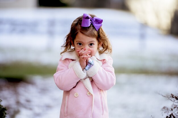 Porträt eines kleinen Mädchens, das in einem Park betet, der im Schnee unter dem Sonnenlicht bedeckt ist