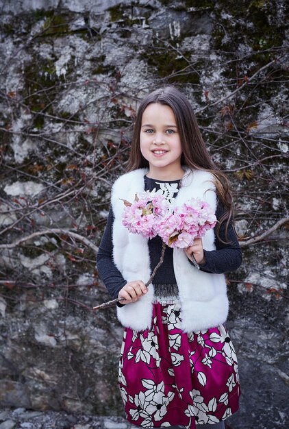 Porträt eines kleinen Mädchens in warmer Kleidung hält einen Blumenstrauß im Freien.