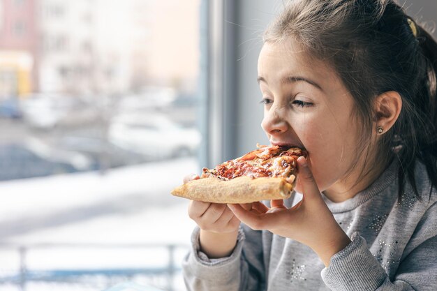 Porträt eines kleinen Mädchens mit einem appetitlichen Stück Pizza