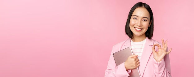 Porträt eines korporativen Frauenmädchens im Büro im Business-Anzug, das ein digitales Tablet hält, das okay reco zeigt