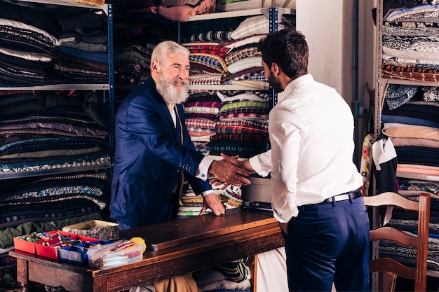 Porträt eines lächelnden älteren männlichen Modedesigners, der Hände mit Kunden in seinem Shop rüttelt