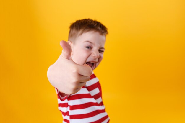 Porträt eines lächelnden aktiven kleinen Jungen, der Daumen hoch zeigt