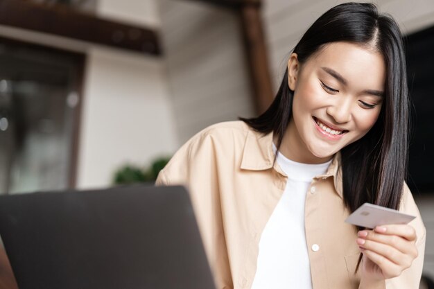 Porträt eines lächelnden asiatischen mädchens, das online mit kreditkarte kauft, die zu hause sitzt und online in...