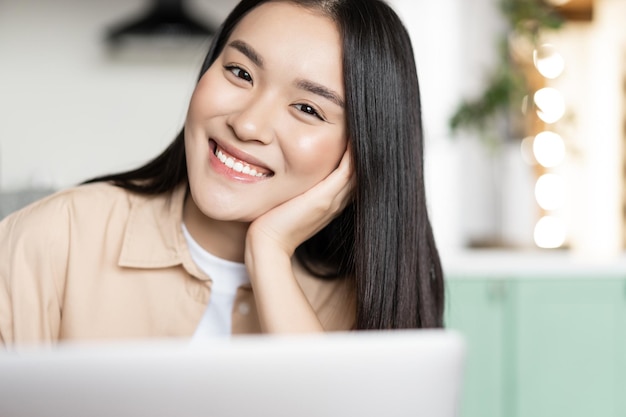 Porträt eines lächelnden asiatischen Studentenmädchens, das einen Computer verwendet, der am Laptop arbeitet oder online studiert?