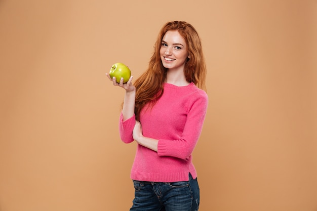 Porträt eines lächelnden hübschen Rothaarigemädchens, das Apfel hält