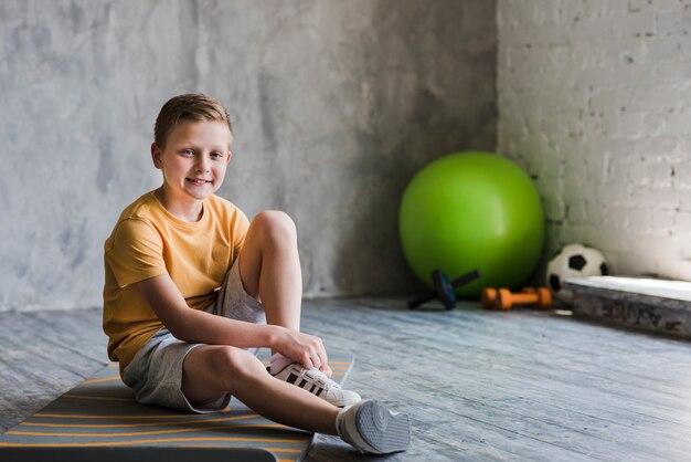 Porträt eines lächelnden Jungen, der auf der Übungsmatte betrachtet Kamera sitzt