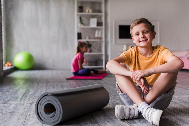 Porträt eines lächelnden Jungen, der nahe der oben gerollten Übungsmatte sitzt