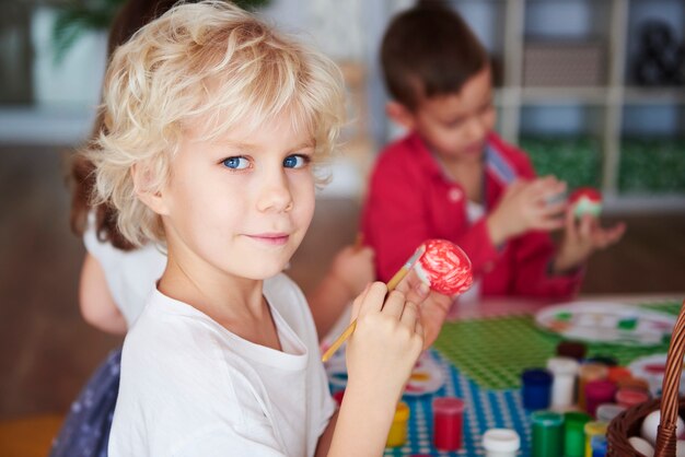 Porträt eines lächelnden Jungen, der Ostereier malt