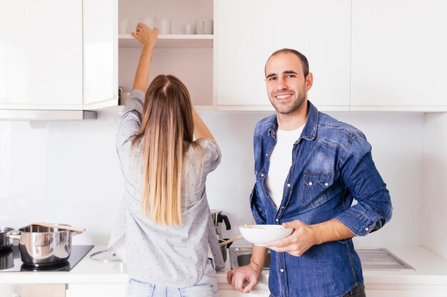 Porträt eines lächelnden jungen Mannes, der Schüssel in den Händen stehen nahe seiner Frau in der Küche hält