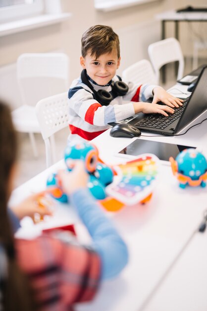 Porträt eines lächelnden Jungen mit Laptop auf dem Schreibtisch, der Kamera betrachtet
