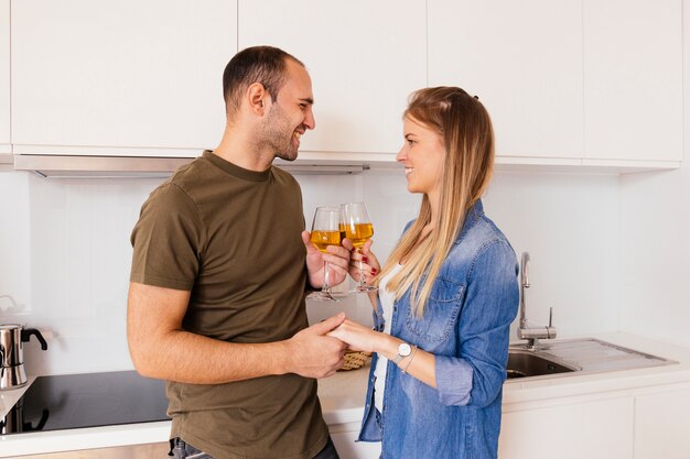 Porträt eines lächelnden jungen Paares, das sich die Hand hält, die die Weingläser in der Küche röstet