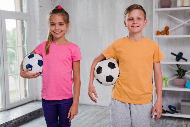 Porträt eines lächelnden Jungen und des Mädchens, die den Fußball betrachtet Kamera hält