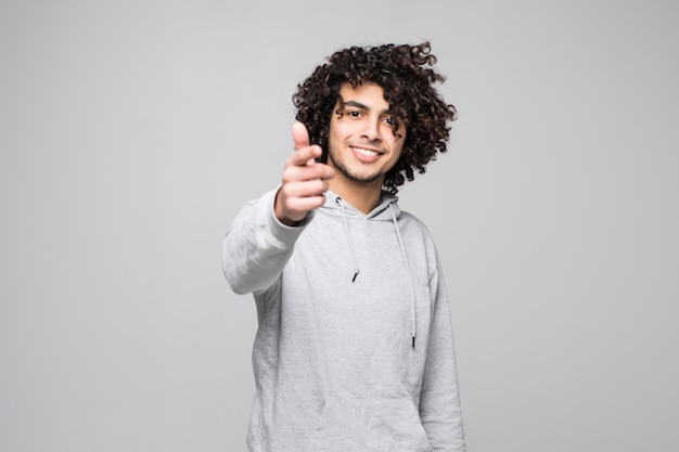 Porträt eines lächelnden lockigen Mannes, der Finger auf Kamera lokalisiert auf einer weißen Wand zeigt