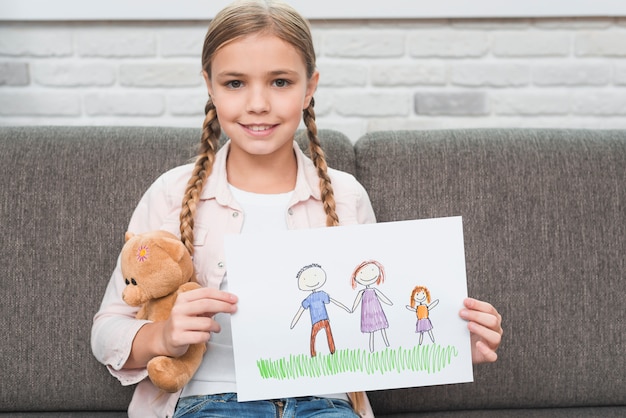 Porträt eines lächelnden Mädchens, das auf dem Sofa zeigt ihre Familienzeichnung auf Papier sitzt