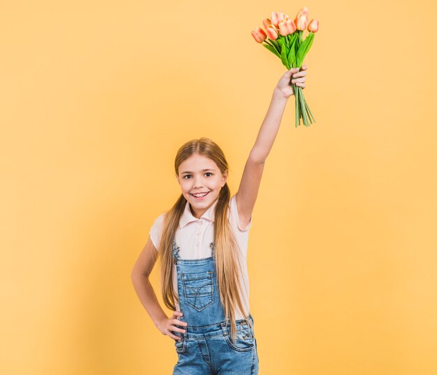 Porträt eines lächelnden Mädchens, das ihre Hand hält Tulpen in der Hand stehen gegen gelben Hintergrund anhebt
