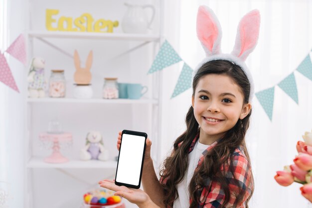 Porträt eines lächelnden Mädchens, das neuen Smartphoneschirm an Ostern-Tag zeigt