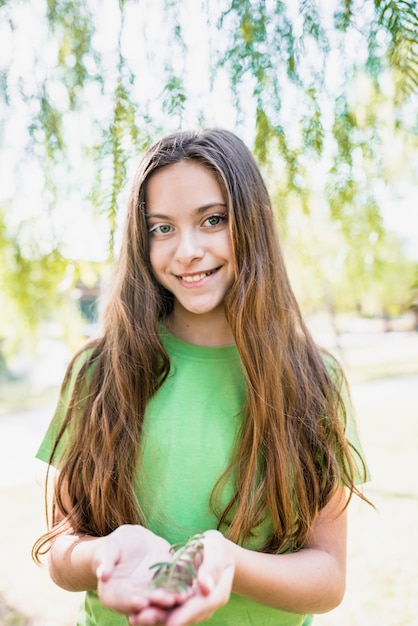 Kostenloses Foto porträt eines lächelnden mädchens mit dem langen haar, das zweig in den händen betrachten kamera hält