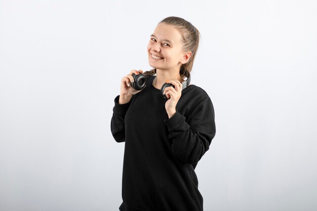 Porträt eines lächelnden Modells des jungen Mädchens, das Kopfhörer in den Händen hält