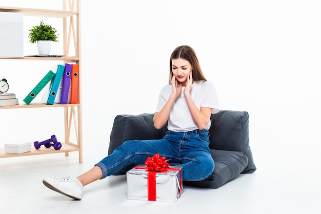 Porträt eines lässigen Mädchens, das auf einem Boden mit Stapel von Geschenkboxen sitzt und weg lokalisiert über weiße Wand schaut