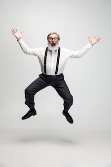 Porträt eines lustigen, fröhlichen professorlehrers des älteren mannes, der isoliert über grauem hintergrund springt