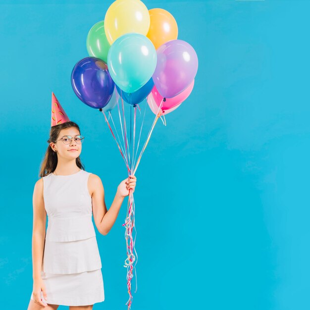 Porträt eines Mädchens, das bunte Ballone auf blauem Hintergrund hält