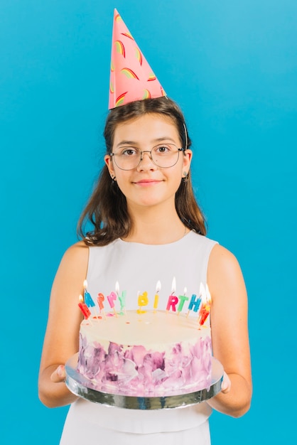 Porträt eines Mädchens, das Geburtstagskuchen auf blauem Hintergrund hält