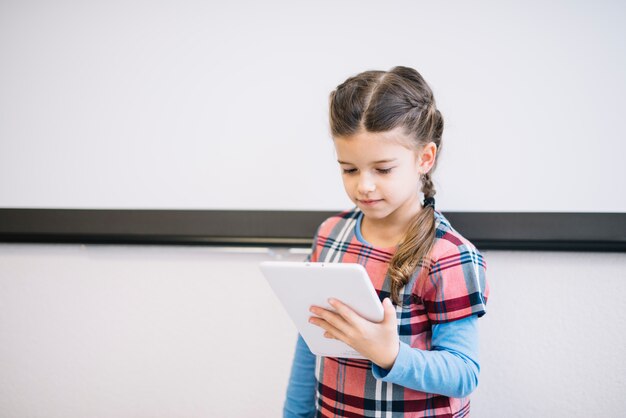 Porträt eines Mädchens, das gegen Wand unter Verwendung der digitalen Tablette steht