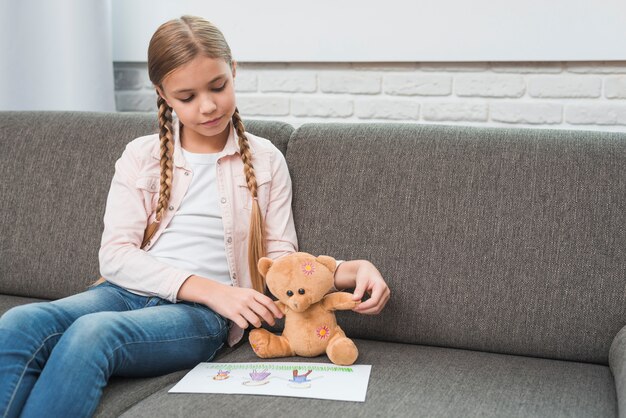 Porträt eines Mädchens, das ihrem Teddybären Familienzeichnungspapier zeigt