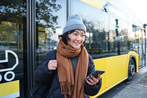 Kostenloses Foto porträt eines mädchens, das in der nähe des busses an einer haltestelle steht und auf ihren fahrplan für öffentliche verkehrsmittel auf sm wartet