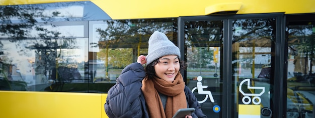 Kostenloses Foto porträt eines mädchens, das in der nähe eines busses an einer haltestelle steht und auf den fahrplan für die öffentlichen verkehrsmittel wartet