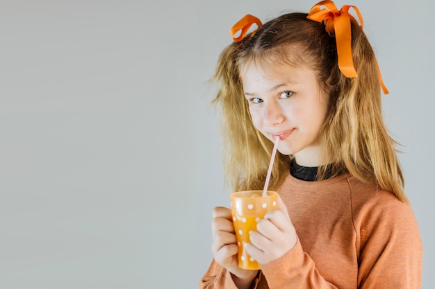 Porträt eines Mädchens, das Saft auf grauem Hintergrund trinkt